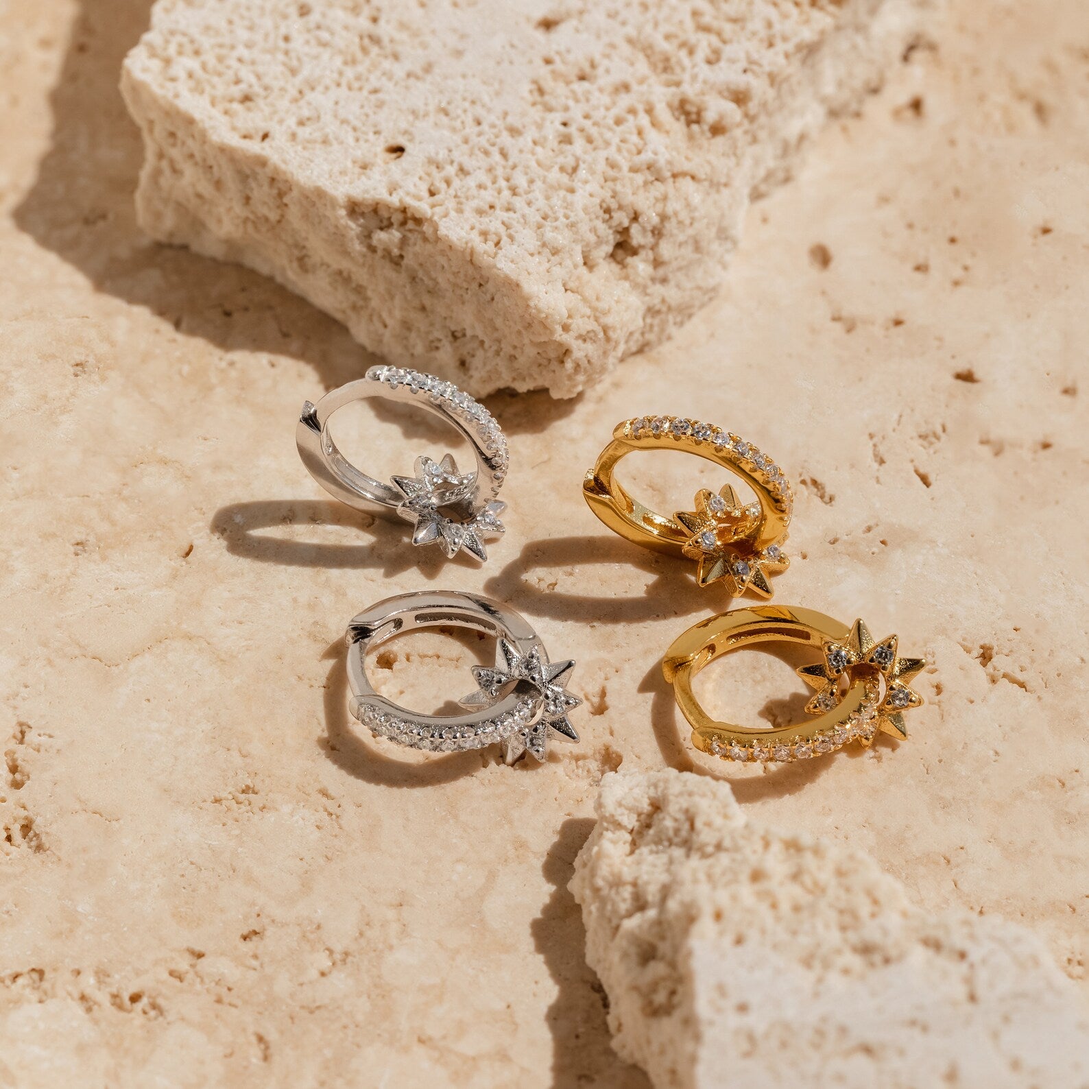 Two pairs of Pave Sun Huggies, one gold and one silver, displayed on light textured stone—a celestial twist on classic hoops.