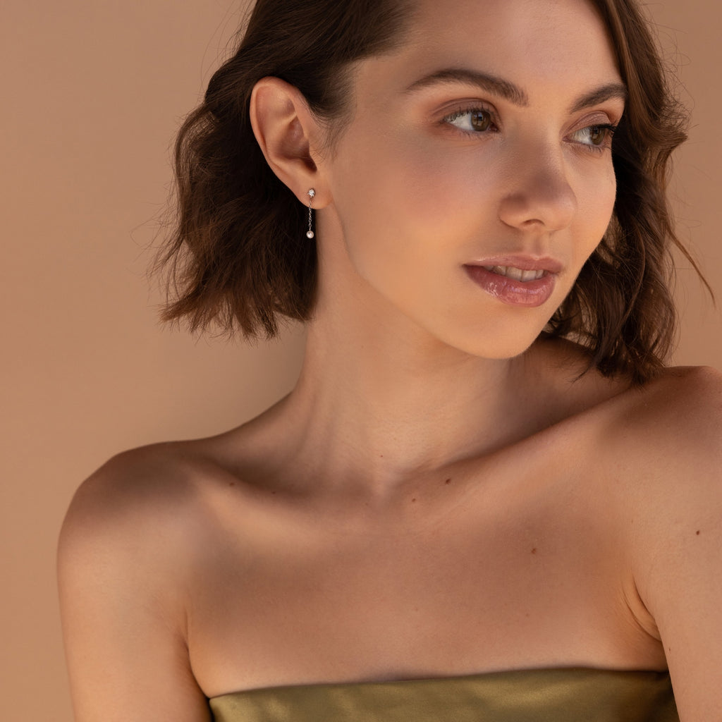 Woman with short brown hair, wearing a strapless olive dress and the Diamond Pearl Drop Earrings, looking to the side.