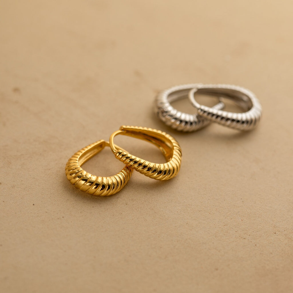 Two pairs of textured hoop earrings, featuring Bold Ribbed Hoops in gold and silver hoops with geometric designs, displayed on a beige surface.