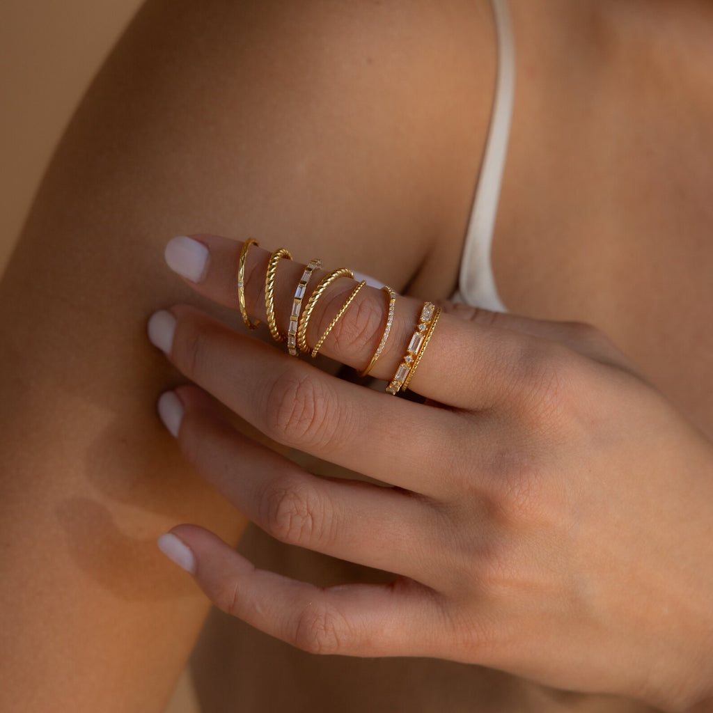 A hand with white nail polish wears the Diamond Stacking Ring Set in 18K Gold, featuring multiple gold stacking rings and a diamond ring, resting on a bare shoulder.