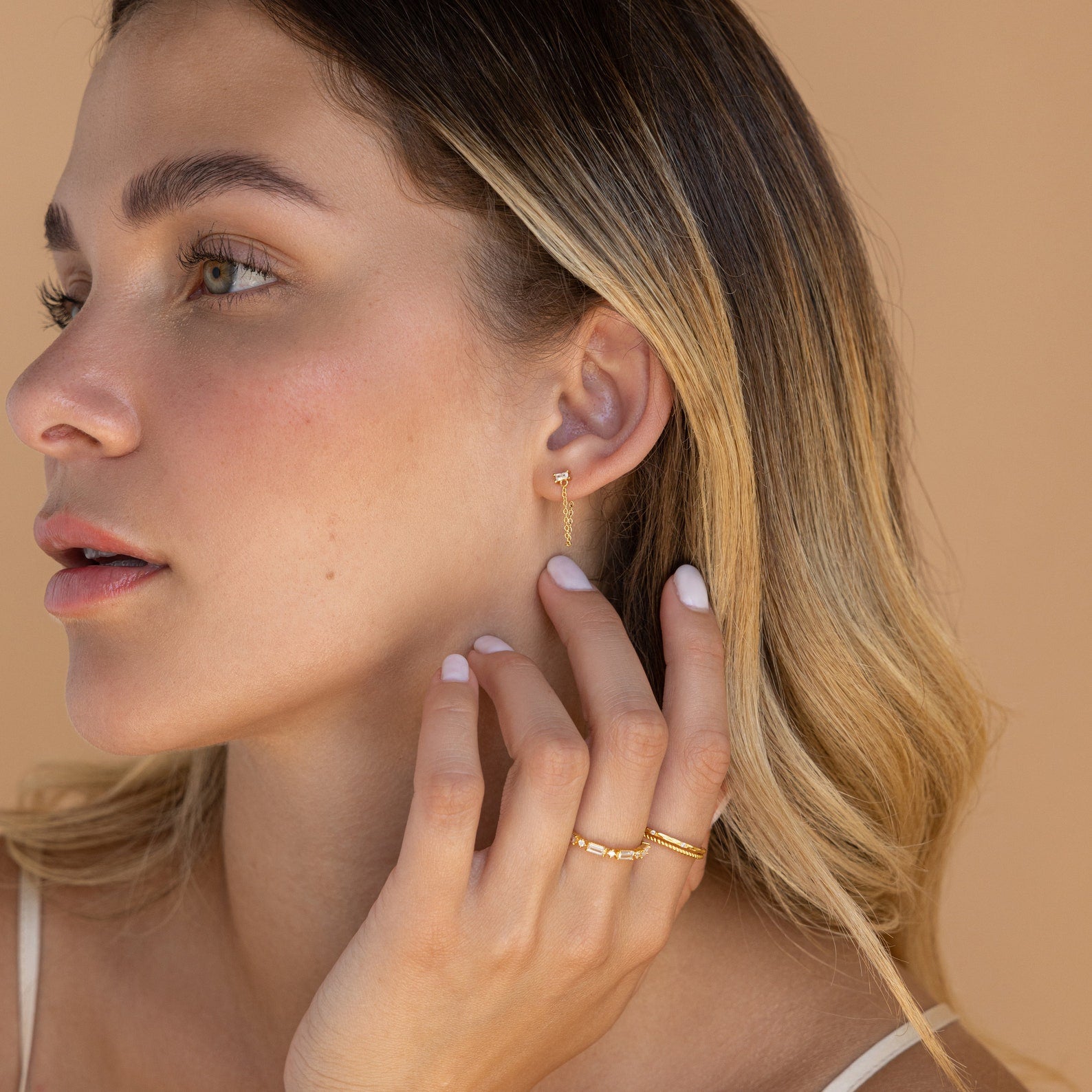 Blonde woman wearing the Diamond Chain Earrings Set touches her ear, highlighting the jewelry against a beige background.