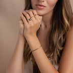 A woman with long hair wears an elegant Black Diamond Tennis Bracelet and gold rings, hands near her face against a neutral background.