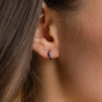 Close-up of a woman's ear wearing Indigo Blue Opal Huggies, minimalist hoop earrings adorned with indigo blue opal stones.