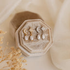 Two pairs of Moon & Star Pearl Earrings, each with delicate pearl charms, are displayed on a beige velvet jewelry box.