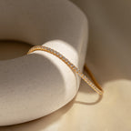 The Classic Diamond Tennis Bracelet in 18K Gold rests on a round, off-white stone, beautifully illuminated by soft natural lighting.