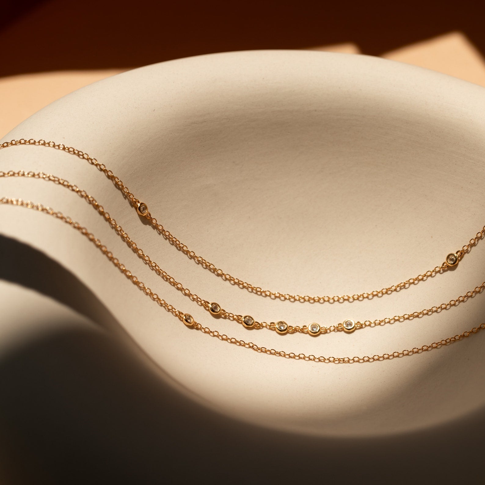Beaded Belly Chains exude bohemian elegance, showcased on a curved beige ceramic surface in soft sunlight.
