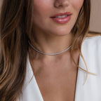 Close-up of a woman wearing a white blouse and a shimmering diamond tennis choker necklace, with soft pink lips and wavy brown hair framing her face.