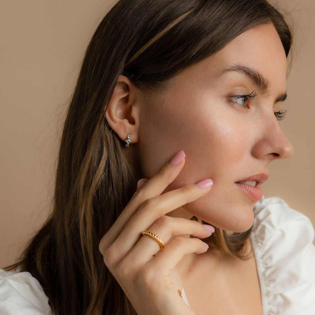 Profile shot of a model wearing the gold Aquamarine Diamond Huggies, with a soft glow on her skin highlighting the blue gemstones.