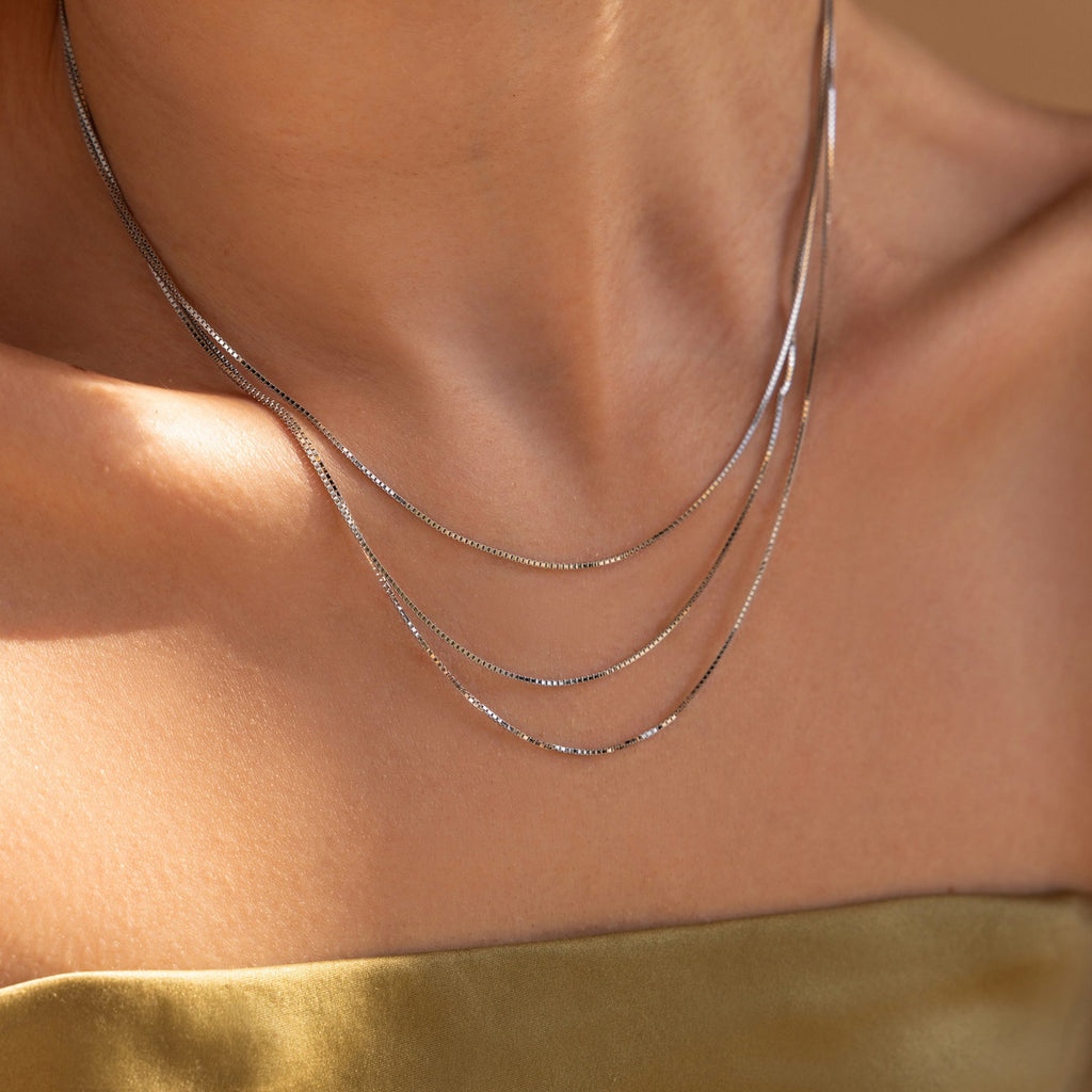 A person wearing the Triple Box Chain Necklace and a gold off-shoulder top in soft lighting.