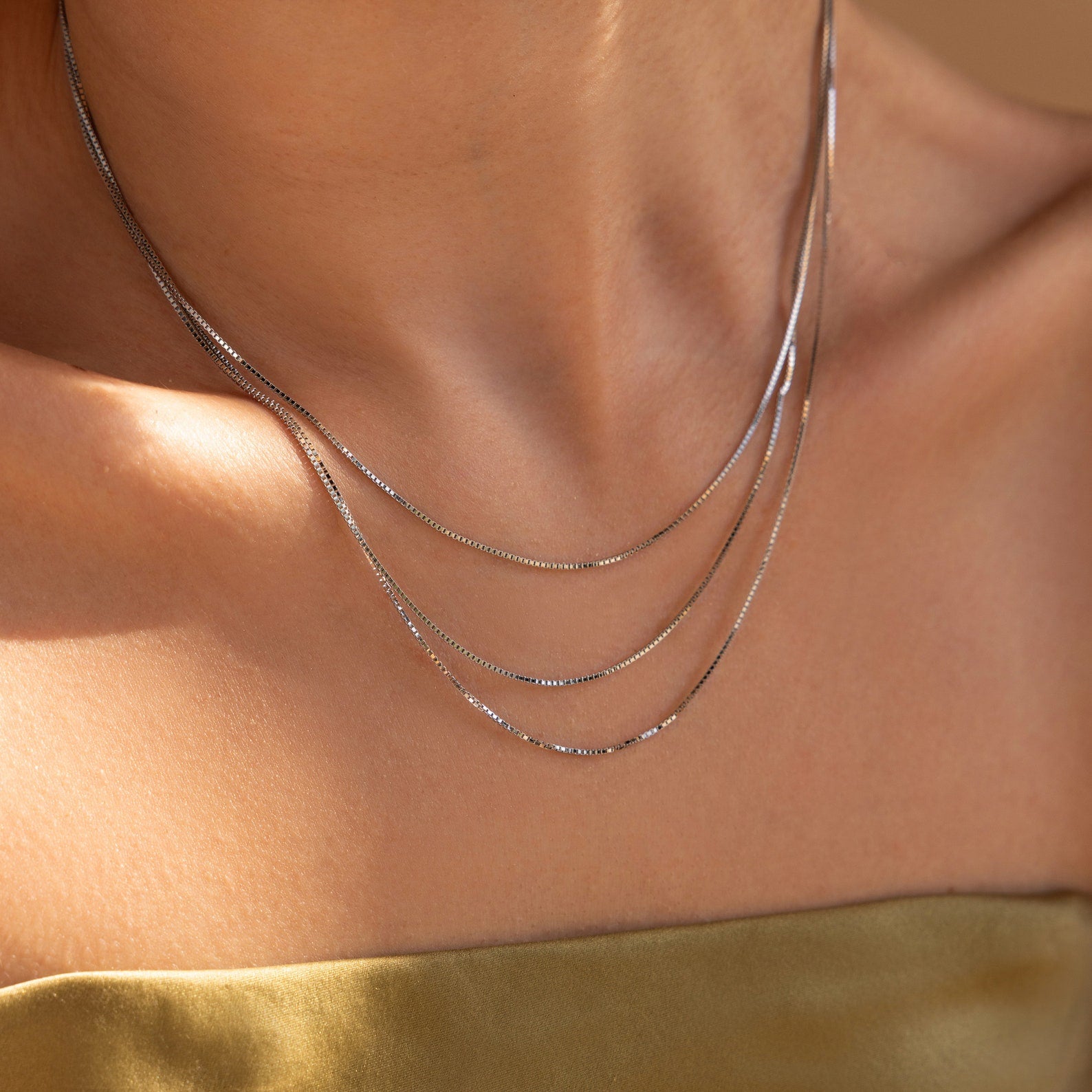 A person wearing the Triple Box Chain Necklace and a gold off-shoulder top in soft lighting.
