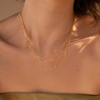 A person wears the Triple Box Chain Necklace, a delicate set of three gold layered necklaces with dainty box chains, elegantly draped on their bare neck and shoulders.