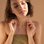 A woman with short brown hair wears a strapless top and the Triple Box Chain Necklace layered with gold pieces, looking down gently.