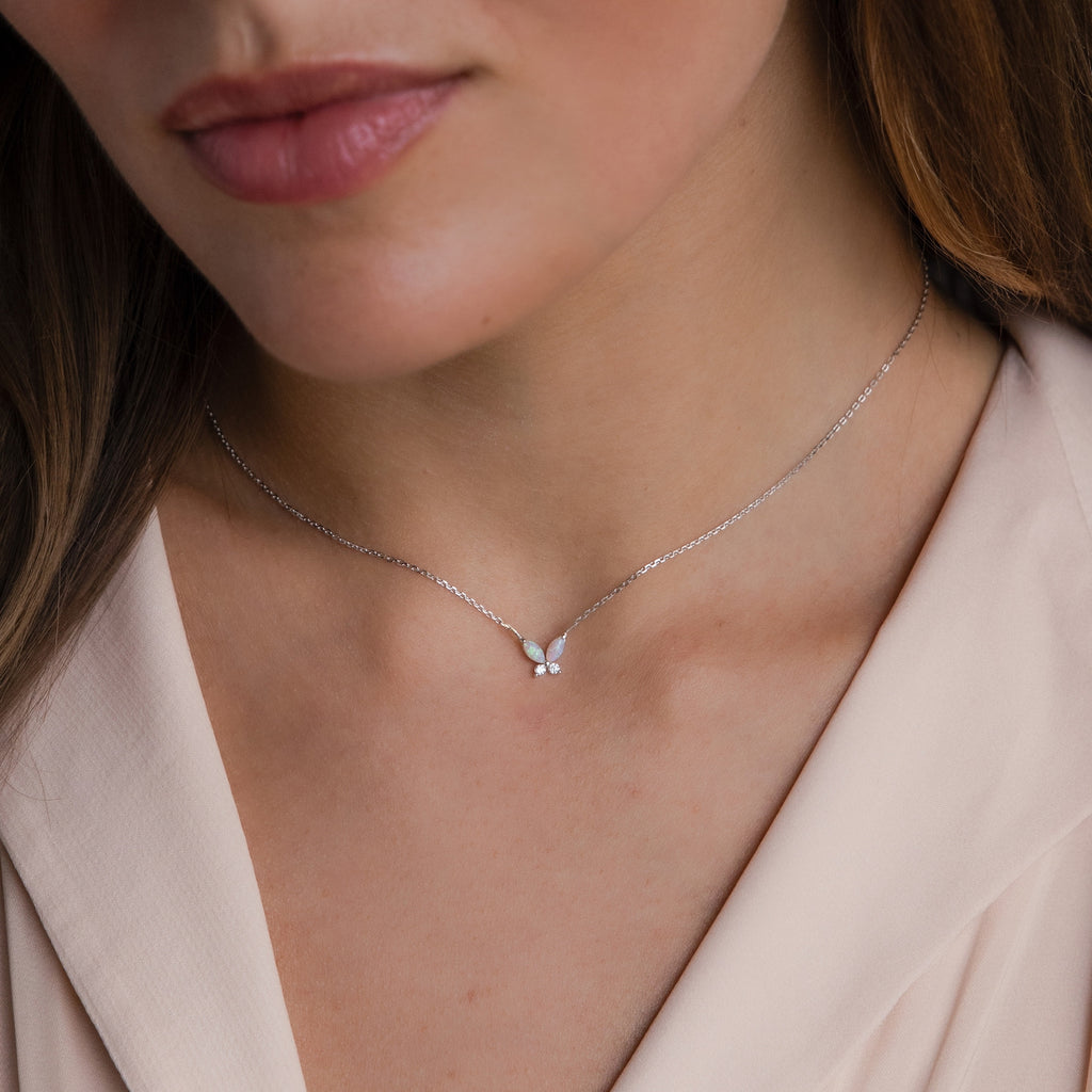 A woman wears the Pink Opal Butterfly Necklace, its petite butterfly pendant adding a delicate charm to her beige blouse.