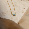 Opal Butterfly Necklace Set with a gold chain and delicate blue opal butterfly pendant, displayed on a light textured stone surface.