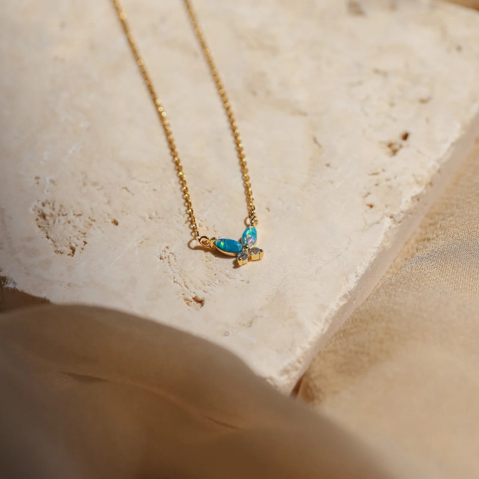 Opal Butterfly Necklace Set with a gold chain and delicate blue opal butterfly pendant, displayed on a light textured stone surface.