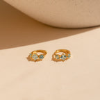 The gold Aquamarine Diamond Huggies displayed flat with their aquamarine stones facing forward on a warm beige background.