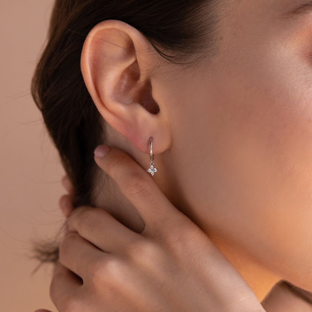 A close-up view of the silver Diamond Flower Huggie worn by a woman. Her ear is turned slightly, and her hand rests gently on her neck, drawing attention to the sparkle of the diamond flower beneath the sleek silver hoop.