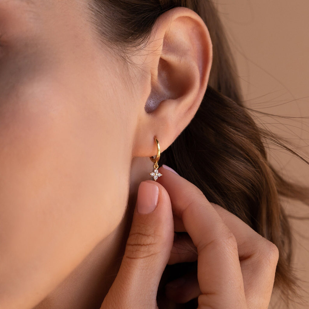 A gold Diamond Flower Huggie earring worn on a woman’s ear, with the small diamond-studded flower charm visible beneath the earlobe. 