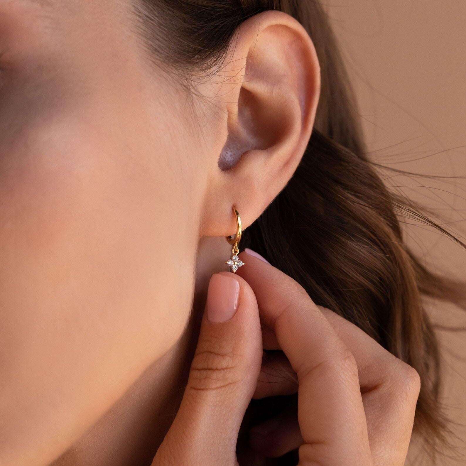A gold Diamond Flower Huggie earring worn on a woman’s ear, with the small diamond-studded flower charm visible beneath the earlobe. 