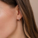 Close-up of a woman wearing Aquamarine Pave Huggies—small, gold hoop earrings accented with sparkling aquamarine stones—as part of a chic earring stack.