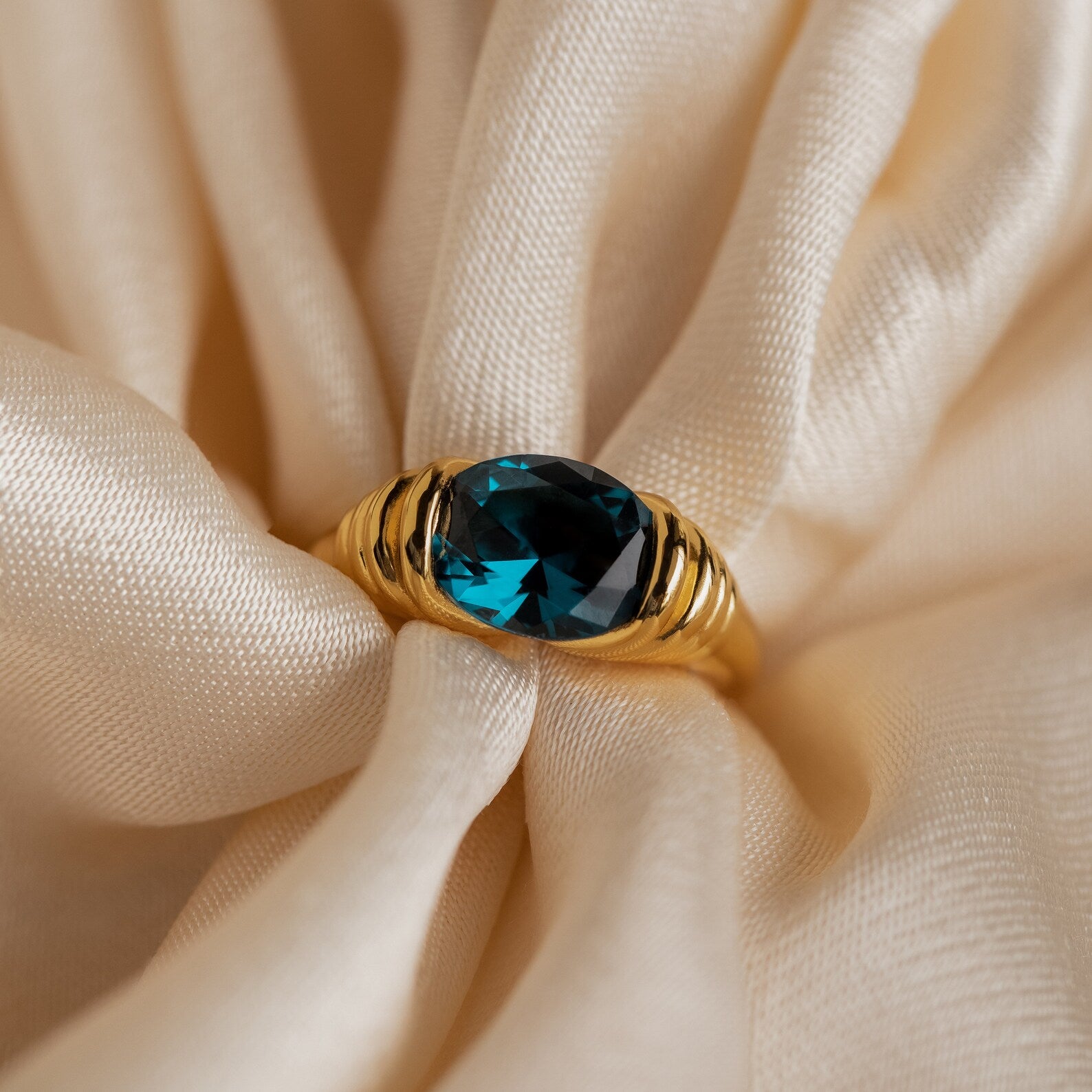 The London Blue Signet Ring features a striking London Blue Topaz gemstone, elegantly showcased on soft, cream-colored fabric with gentle folds.