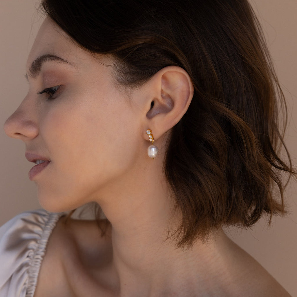 Profile view of a model wearing the gold Millie Drop Earrings with her hair tucked behind her ear.