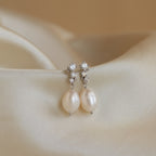 Silver Millie Drop Earrings displayed on satin fabric, with round-cut stones and freshwater pearls in soft lighting.