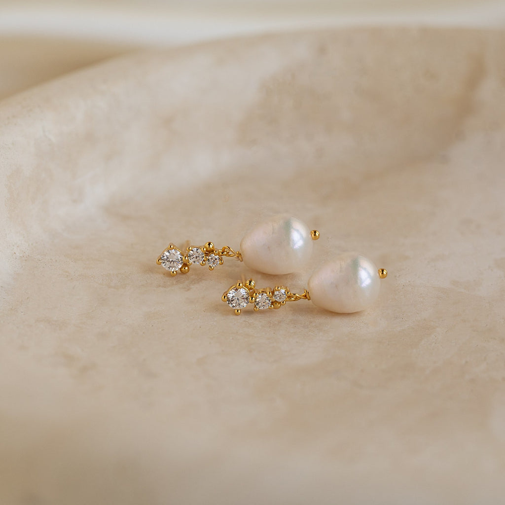Gold Millie Drop Earrings laid flat, showcasing the cubic zirconia detail and baroque pearls.