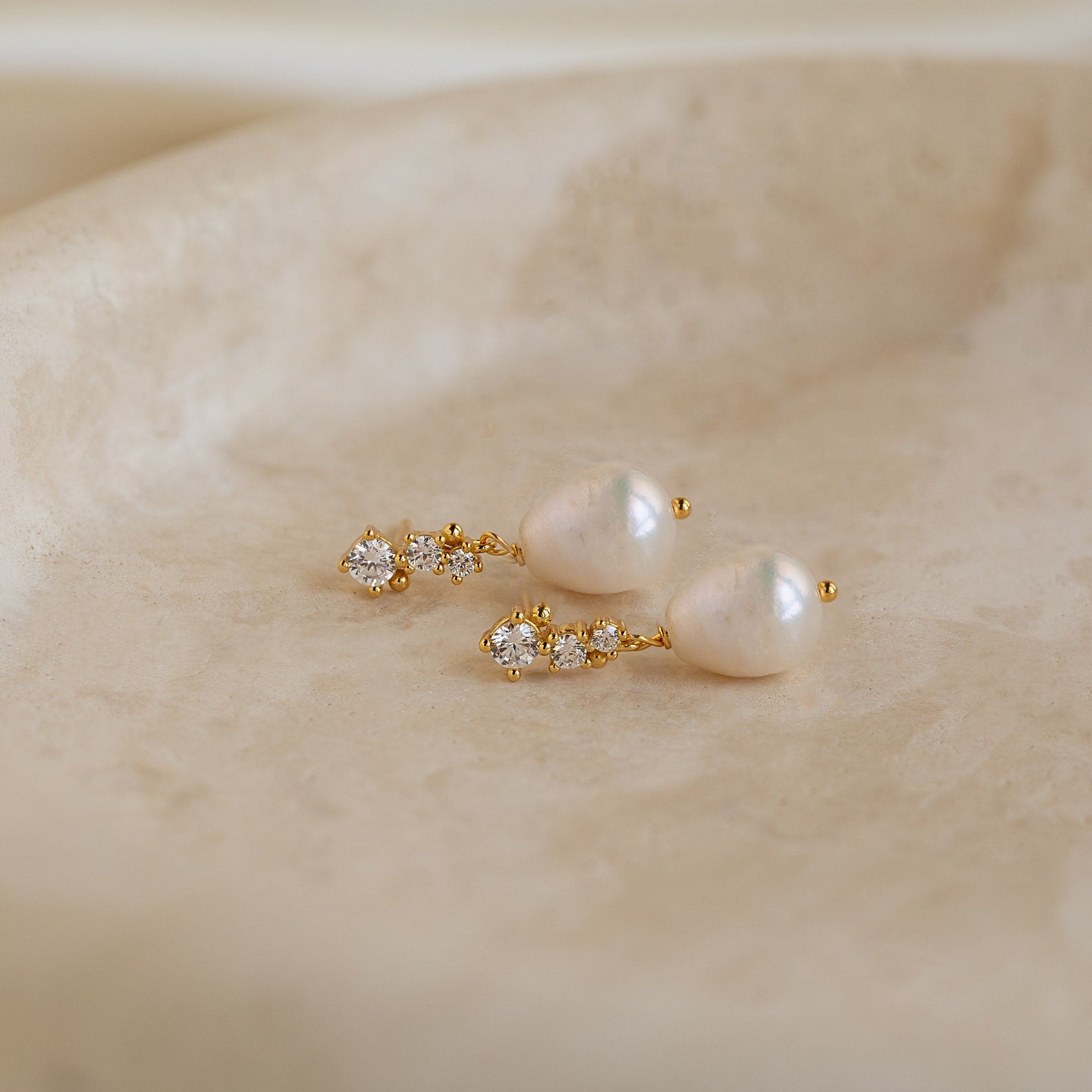 Gold Millie Drop Earrings laid flat, showcasing the cubic zirconia detail and baroque pearls.