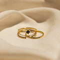 Three gold rings with small black gemstones from the Black Abyss Ring Set displayed on soft beige fabric.