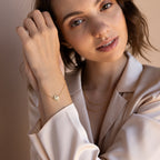 Woman in a satin blouse models the Carrie Initial Bracelet, featuring a delicate gold monogram charm—an elegant personalized jewelry piece.
