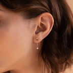 Close-up of a woman's ear wearing Diamond Pearl Drop Earrings—a gold earring with a small pearl hanging from a thin chain, perfect for fans of elegant dangling stud earrings.