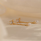 Diamond Pearl Drop Earrings feature sparkling diamonds and pearls on gold chains, beautifully displayed against a soft beige fabric background.