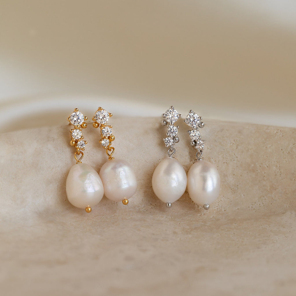 Side-by-side display of both gold and silver versions of Millie Drop Earrings on a stone surface.