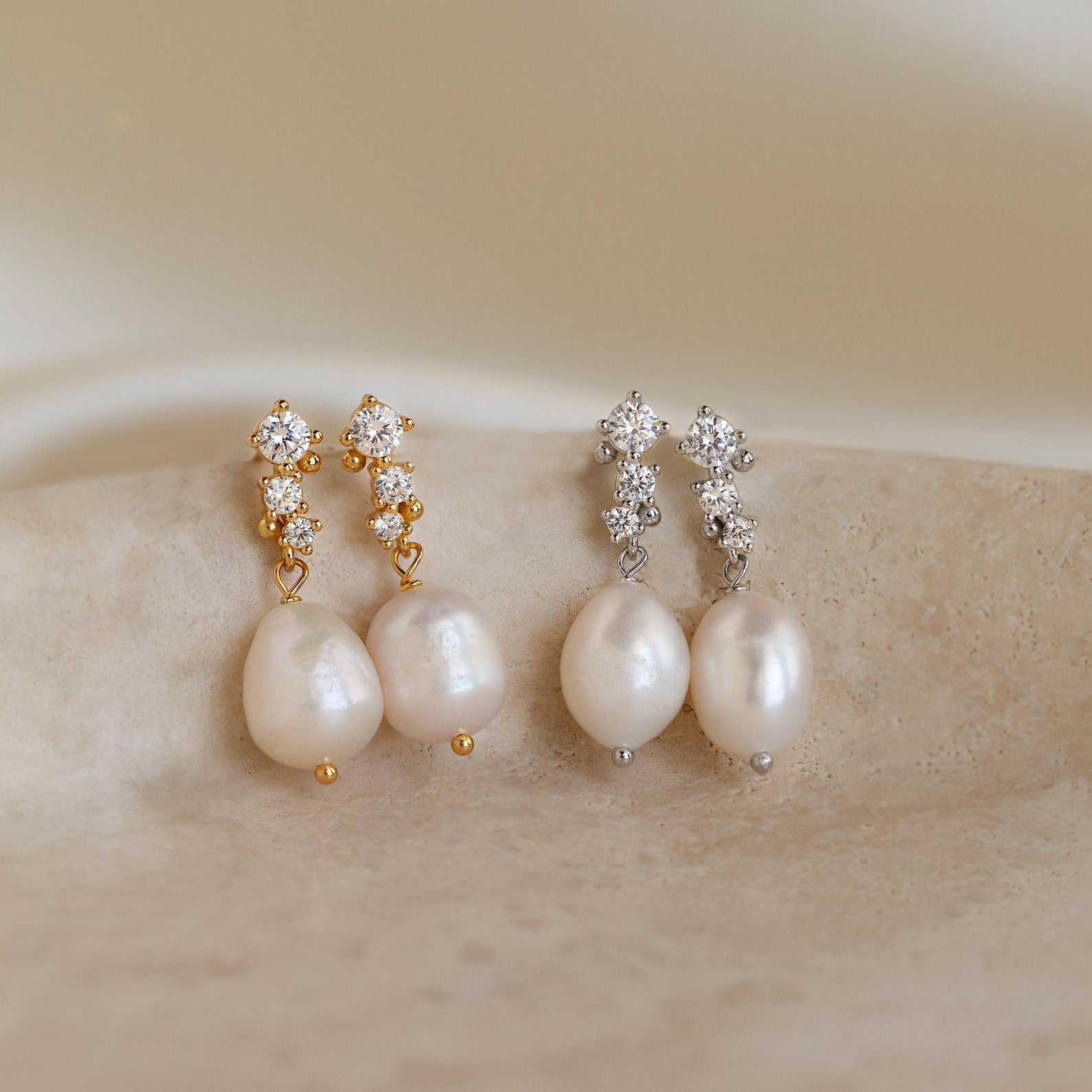 Side-by-side display of both gold and silver versions of Millie Drop Earrings on a stone surface.