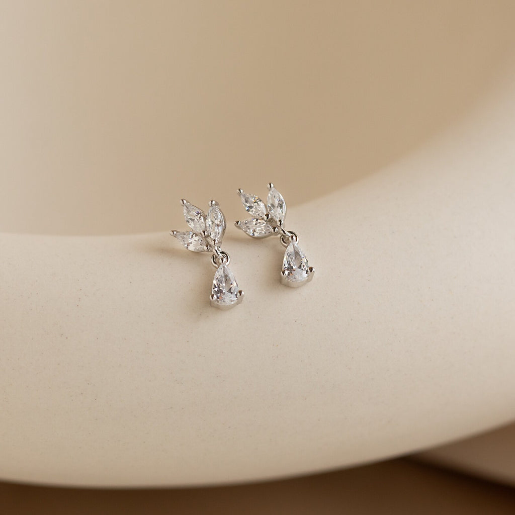 The Marquise Diamond Drop Studs, featuring leaf-shaped and marquise-cut diamonds in a silver teardrop design, rest on a smooth beige background.