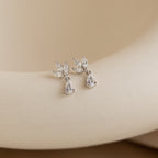 The Marquise Diamond Drop Studs, featuring leaf-shaped and marquise-cut diamonds in a silver teardrop design, rest on a smooth beige background.