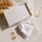 Gold jewelry featuring Marquise Diamond Drop Studs with a matching necklace is displayed next to a white Caitlyn Minimalist gift box and pouch on a light cloth.