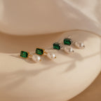 The Emerald Pearl Drop Earrings, featuring both gold and silver styles with green gemstones and pearls, are displayed on a neutral background.