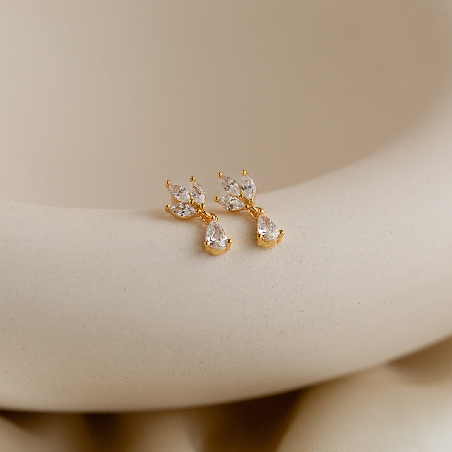 Marquise Diamond Drop Studs featuring clear, marquise-cut gemstones, displayed on a smooth cream-colored surface.