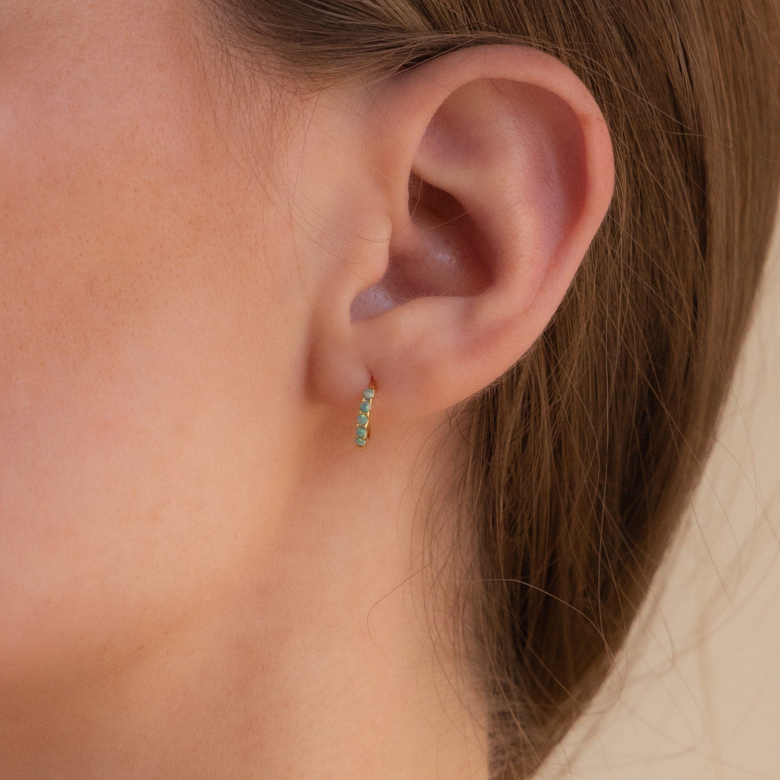 A close-up of a woman's ear adorned with an elegant earring stack, featuring the Garden Green Opal Huggies and green gemstone hoop earrings.