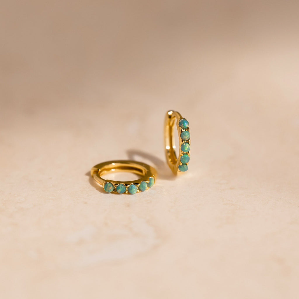 Garden Green Opal Huggies—two gold hoop earrings adorned with small green opal stones, ideal for stacking, displayed on a light beige surface.