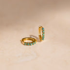 Garden Green Opal Huggies—two gold hoop earrings adorned with small green opal stones, ideal for stacking, displayed on a light beige surface.