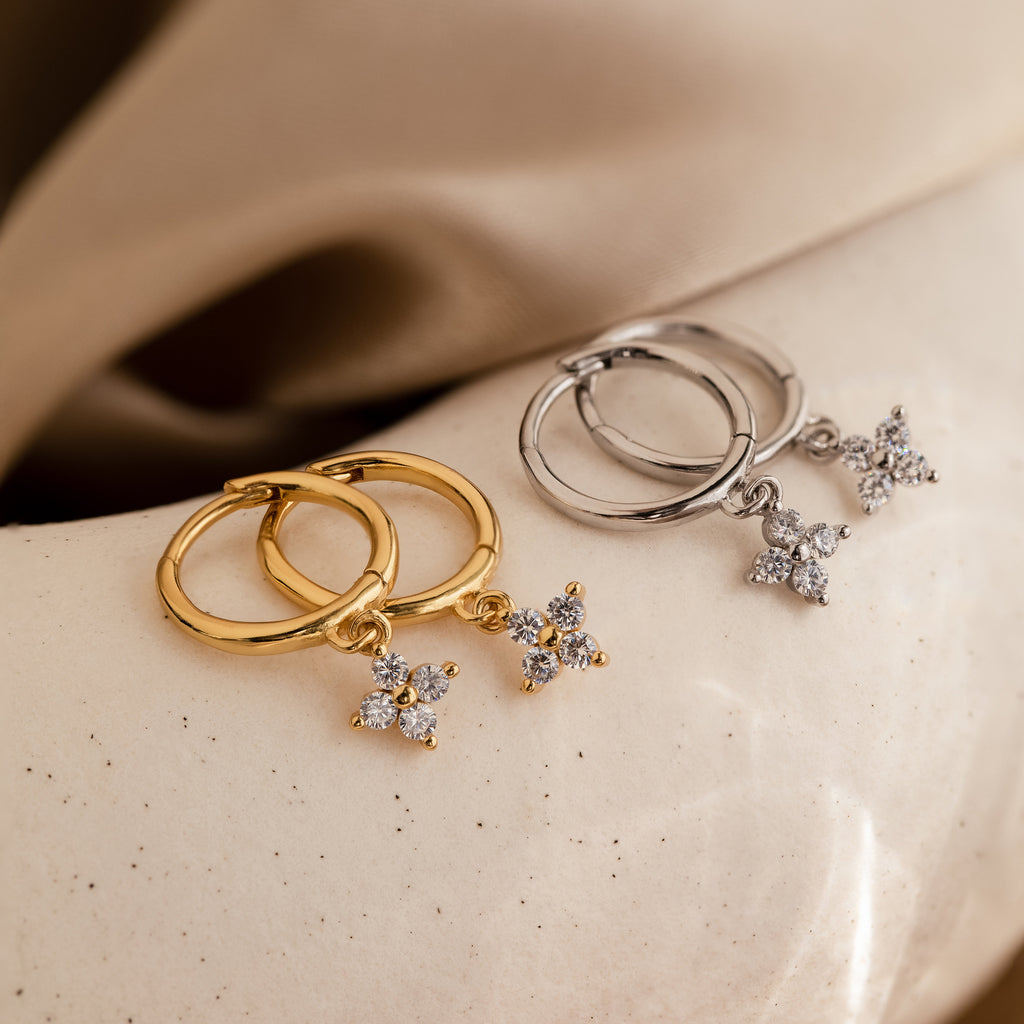 Two pairs of Diamond Flower Huggies—one in gold, one in silver—displayed on a soft neutral surface