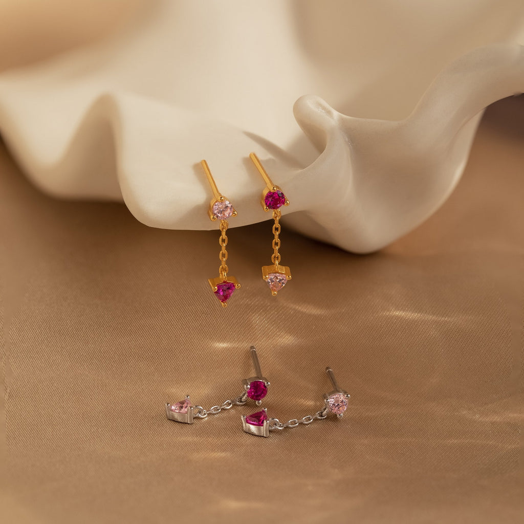 Mixed Pink Drop Earrings—romantic gold and silver earrings with pink gemstones—are displayed on a soft beige background with a shell prop.