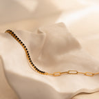 The Black Diamond Tennis Bracelet showcases stunning black diamonds set on a gold chain, making it an elegant statement piece for any occasion.