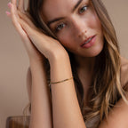 A woman with long brown hair leans her head on her hands, showcasing the elegant Black Diamond Tennis Bracelet—a stunning statement piece—set against a beige background.