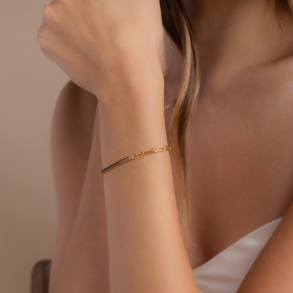 A woman wearing a Black Diamond Tennis Bracelet—an elegant gold piece with small black beads—on her wrist, dressed in a white top.