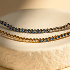 The Blue Diamond Tennis Bracelet features alternating blue and clear stones set in classic silver, making it a minimalist accessory and the perfect “something blue” for your look, elegantly displayed on a textured surface.