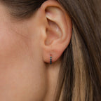 Close-up of a woman's ear wearing Indigo Blue Opal Huggies—minimalist gold hoop earrings accented with indigo blue opal stones.